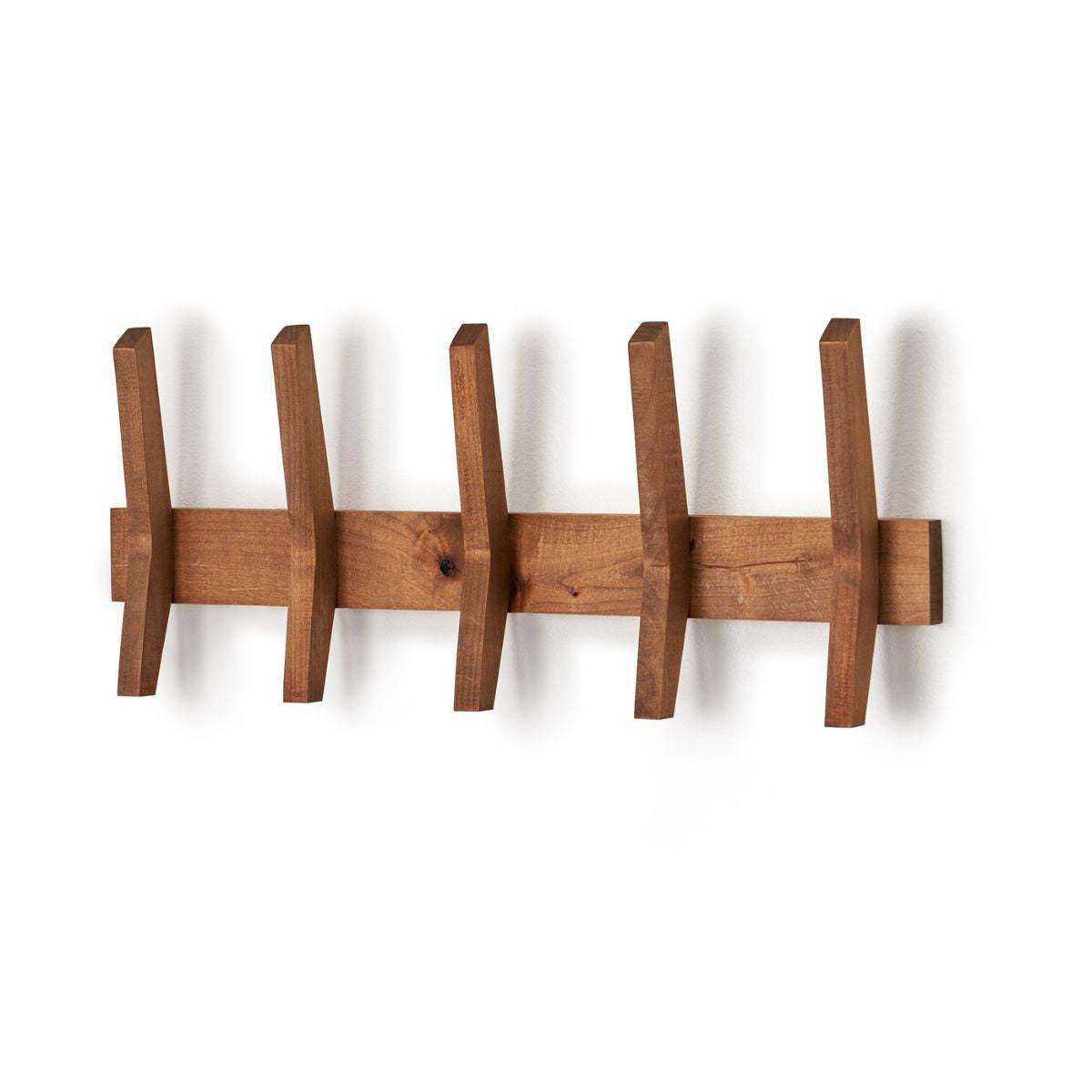 A wall-mounted wooden coat rack features five angled wooden hooks evenly spaced along a horizontal wooden bar. The coat rack casts a soft shadow on the white wall behind it.