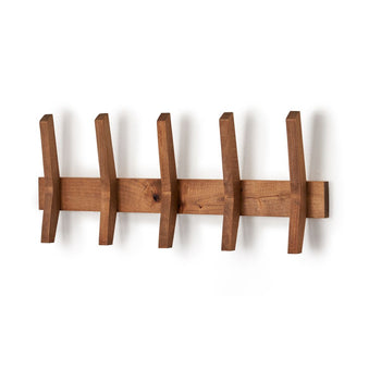 A wall-mounted wooden coat rack features five angled wooden hooks evenly spaced along a horizontal wooden bar. The coat rack casts a soft shadow on the white wall behind it.