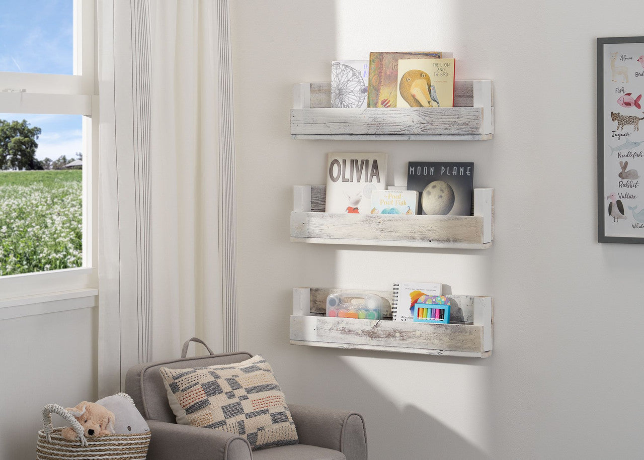 Three-tiered set of floating nursery shelves in rustic whitewashed wood are mounted on a white wall in a child's room. Each shelf displays different books and decorative items.