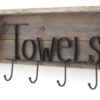 A close-up shows a rustic wooden towel rack mounted on a white wall. The rack features the word 