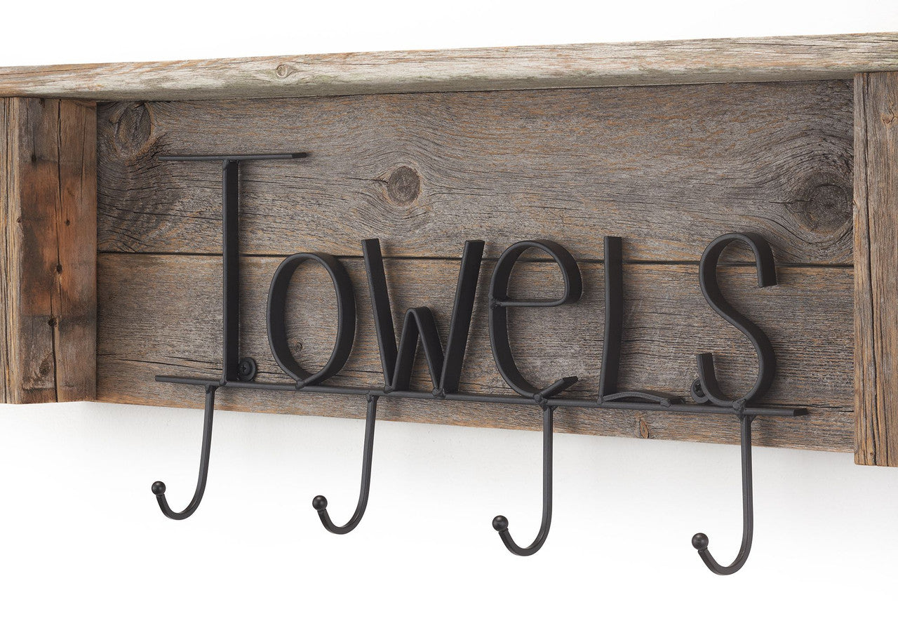 A close-up shows a rustic wooden towel rack mounted on a white wall. The rack features the word "Towels" spelled out in black metal lettering above four hanging hooks.