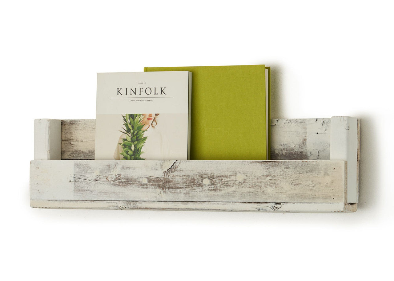A white, rustic wooden shelf is mounted on a white wall, holding a magazine titled "KINFOLK" and a green book. The shelf is made from reclaimed wood and has a simple, rectangular design with a slightly distressed finish.