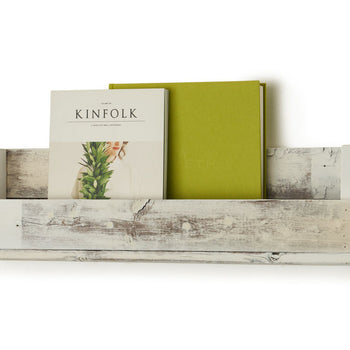 A white, rustic wooden shelf is mounted on a white wall, holding a magazine titled 