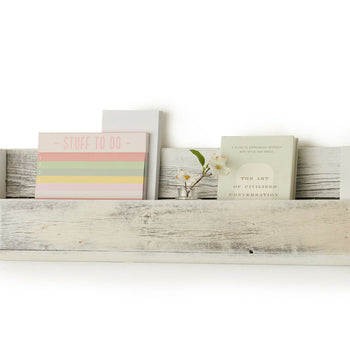 A white wooden shelf with a rustic, weathered finish is mounted on a white wall, holding a notepad titled 