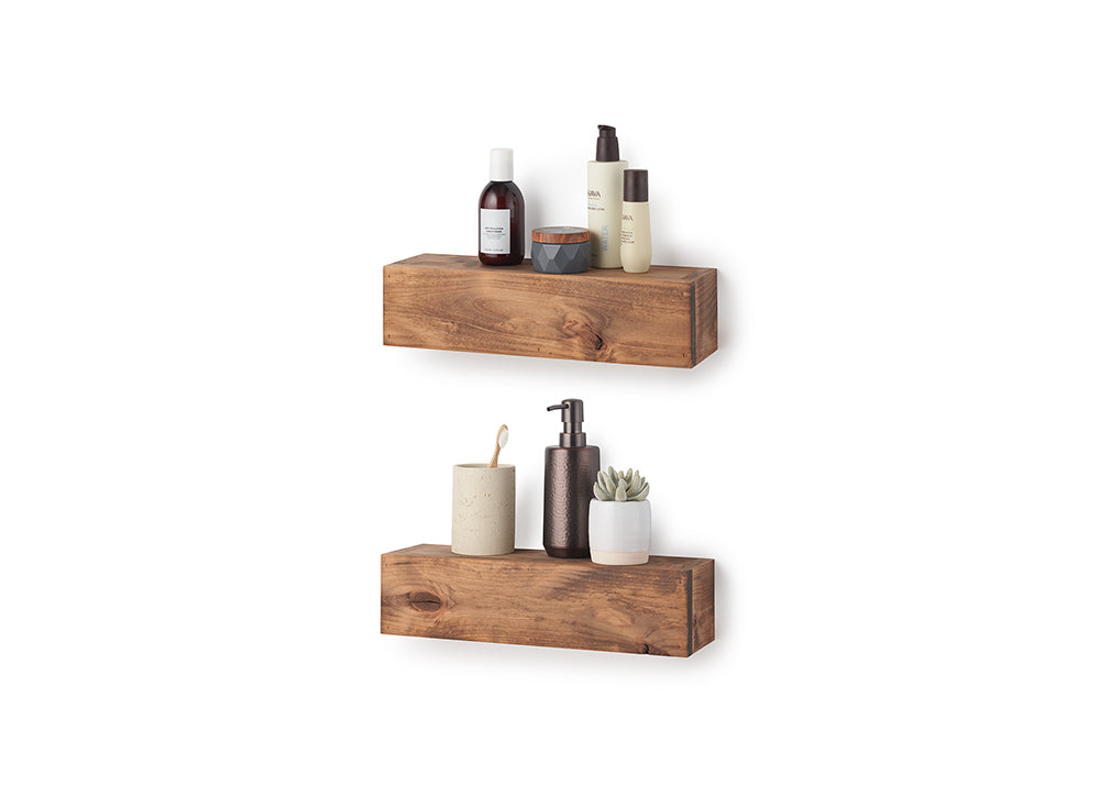 Two floating shelves made of chunky, natural-grained wood are mounted on a white wall and hold various bathroom essentials. The top shelf displays skincare bottles and a small jar, while the bottom shelf holds a toothbrush in a cup, a soap dispenser, and a tiny potted succulent.