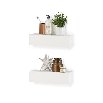 Two minimalist white floating box shelves are mounted vertically on a plain white wall, each holding various decorative and personal care items. The top shelf features a wooden toothbrush holder, a bottle of hand soap, and a small potted green plant, while the bottom shelf displays two starfish, a brown glass jar, and a small tin.