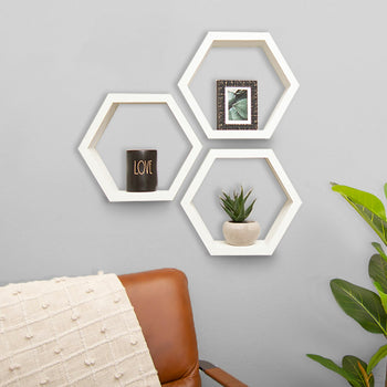 Three honeycomb-shaped shelves in white wood are mounted on a textured gray wall, holding a small black candle with the word 
