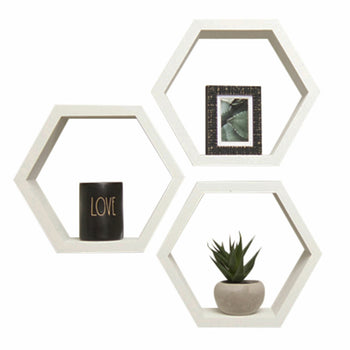 Three white hexagon shelves are mounted on a white wall, each containing a different item: a framed picture, a black container labeled 