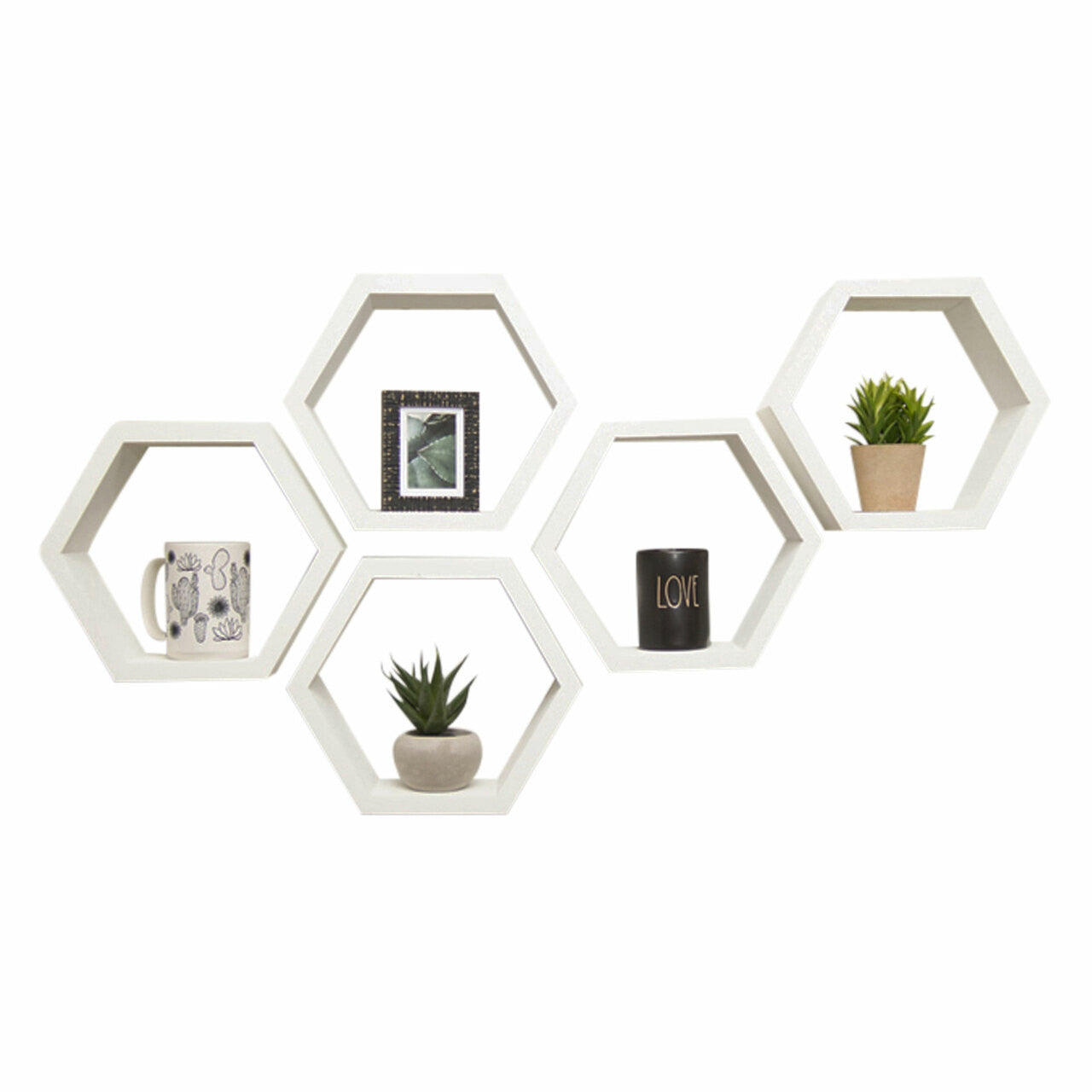 A set of five white hexagon floating shelves are mounted on a white wall in a staggered arrangement. Each shelf holds a small decorative item, including a framed picture, a potted plant, a mug, and a candle that spells the word "LOVE".