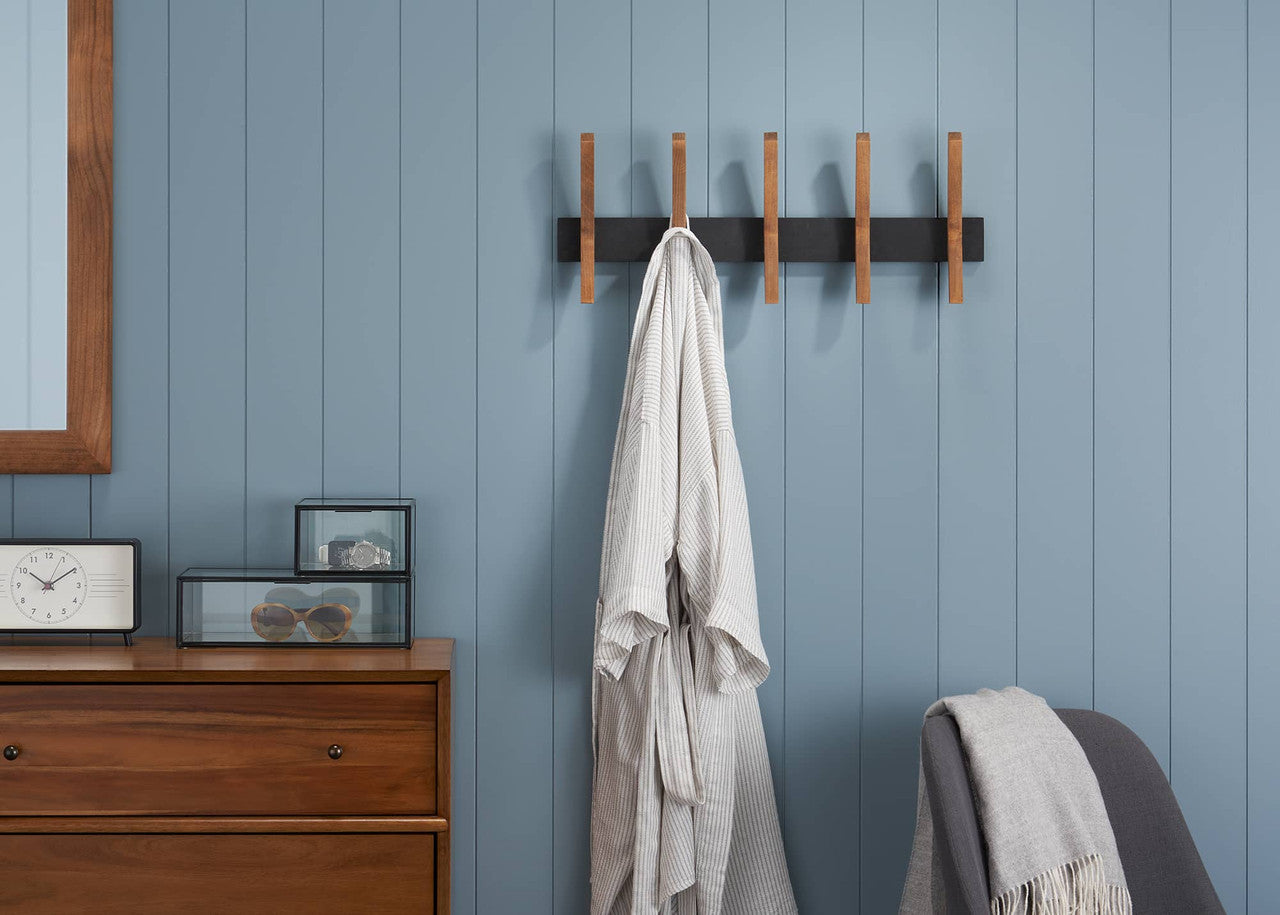 A horizontal black rack with five retractable wooden pegs is mounted on a light blue paneled wall. A white bathrobe hangs from the second peg from the left.