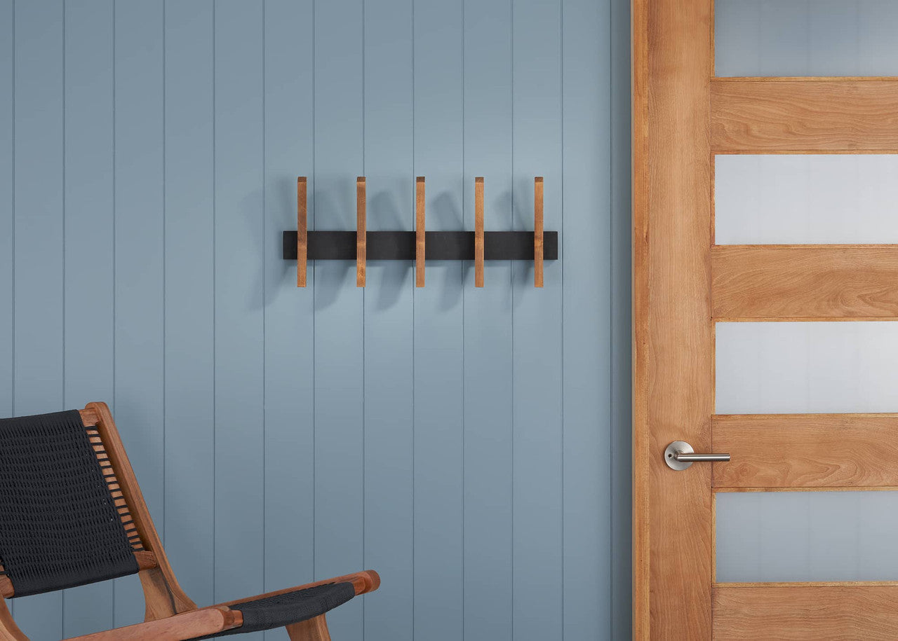 A Mid-Century Coat Rack mounted on a blue wall. The coat rack features a black base with wooden pegs, positioned next to a wooden door with frosted glass panels.
