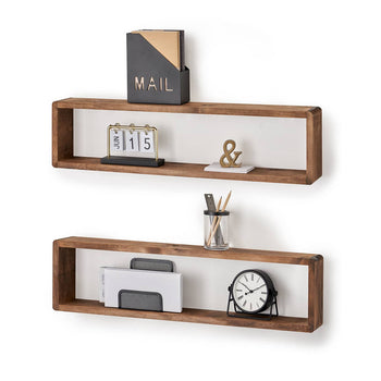 Two rectangular wooden floating shelves with white backings are mounted on a white wall. The top shelf holds a black and gold mail organizer, a small calendar displaying 