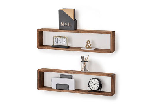 Two rectangular wooden floating shelves with white backings are mounted on a white wall. The top shelf holds a black and gold mail organizer, a small calendar displaying "JUN 15", and a gold ampersand on a white coaster, while the bottom shelf holds a wire document holder with papers, a glass jar with pencils, and a small round clock.
