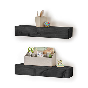 Two dark, rectangular floating shelves are mounted on a white wall, displaying small office supplies. The top shelf holds a cup with pencils and a colorful rubber band ball, while the bottom shelf features a light-colored organizer filled with stationary, and a small stack of sticky notes with a metallic gold decoration.