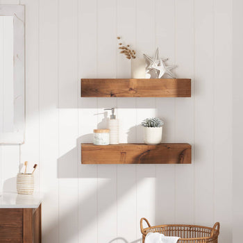 A bathroom with white paneled walls features two wooden floating shelves holding decorative items like a potted plant, soap dispenser, and silver star ornaments. Natural light streams in from an open window, illuminating the space with a cozy, rustic aesthetic.
