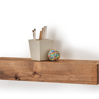 A solid wood floating shelf is mounted on a white wall, holding a small potted plant and a colorful ball. The shelf has a natural wood grain finish and a simple, rectangular design.