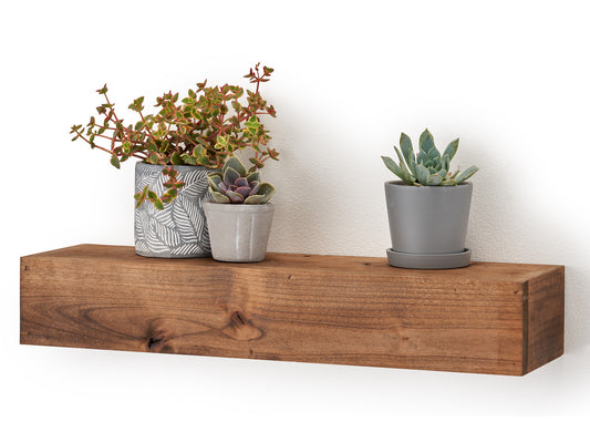 A rustic, solid wood floating shelf adds a touch of natural warmth to a minimalist white wall. Three small succulent planters are arranged on the shelf.