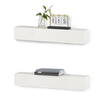 Two rectangular white floating shelves are mounted one above the other against a white background. The top shelf holds a small glass vase with a green sprig and a gold and black flip calendar displaying 