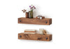 Two rustic wooden floating shelves are mounted on a white wall, each featuring two decorative metal studs on the front. The top shelf holds small vases with flowers, a wooden box with jewelry, while the bottom shelf has stacked books, a candle, and a small wooden container with a lid.