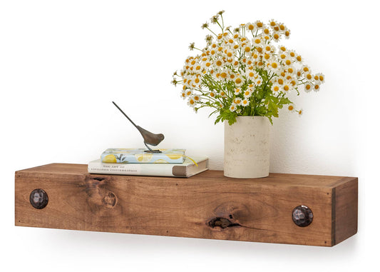 A wooden floating shelf holds a small stack of books titled "THE ART OF CIVILIZED CONVERSATION," with a small bird figurine perched on top, and a vase of white and yellow flowers. The shelf is rustic, made of thick wood with a natural edge and metal accents on the wall mounts.