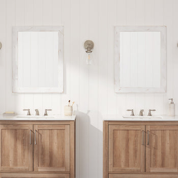 Two identical bathroom vanities with a transitional design are featured, each with a white countertop, undermount sink, and light wood-look cabinets.  The vanities are separated by a small gap and flanked by textured white walls with vintage-inspired sconces and framed mirrors.