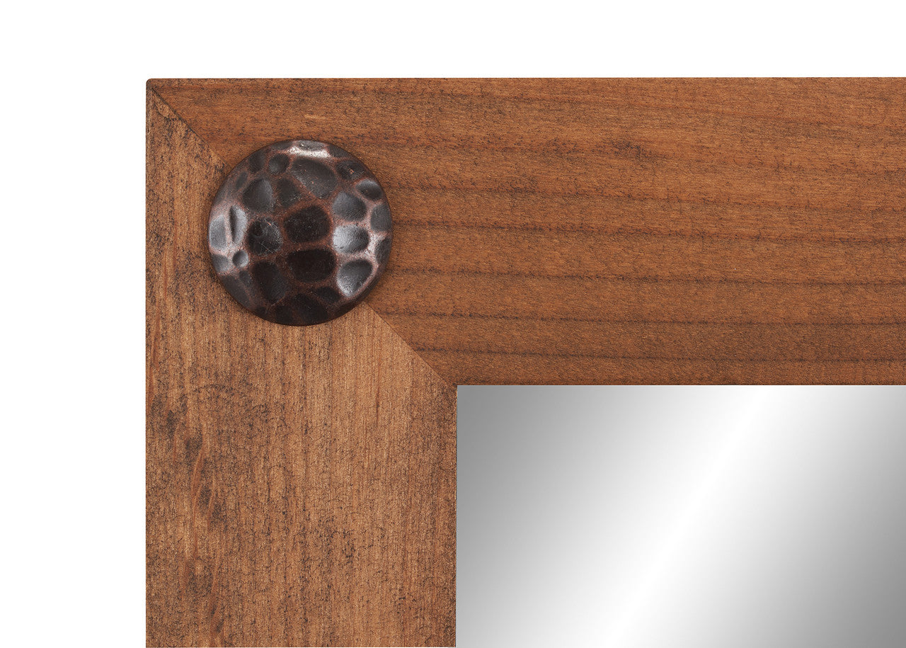 A close-up shot of the corner of a walnut-colored farmhouse vanity mirror, showing the wood grain and a decorative clavos (nail head) detail.