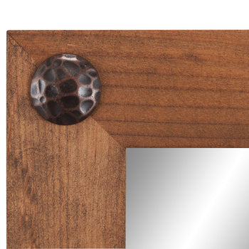 A close-up shot of the corner of a walnut-colored farmhouse vanity mirror, showing the wood grain and a decorative clavos (nail head) detail.