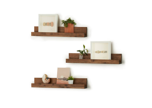 A set of three rustic, reclaimed wood shelves are mounted on a white wall, each holding a picture frame and small potted plants. The shelves have a unique, staggered design with varying depths and lengths.
