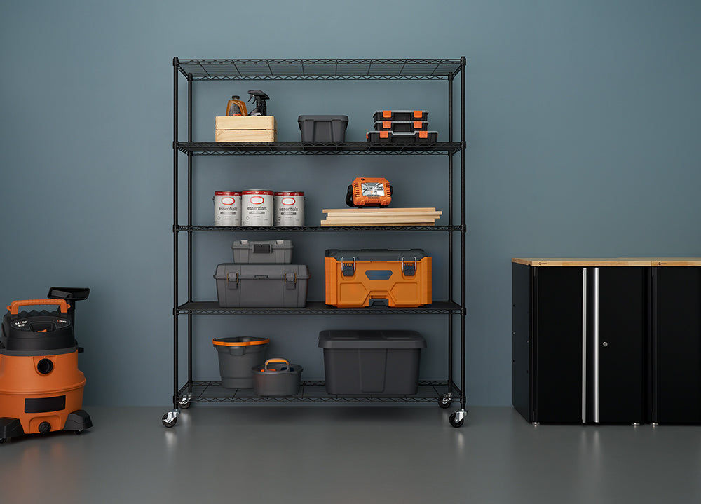 A tall, five-shelf black wire shelving unit with casters is stocked with various storage bins, toolboxes, paint cans, and other garage or workshop supplies against a blue wall. To the left is an orange and black shop vacuum, and to the right is a black storage cabinet with a wood top.