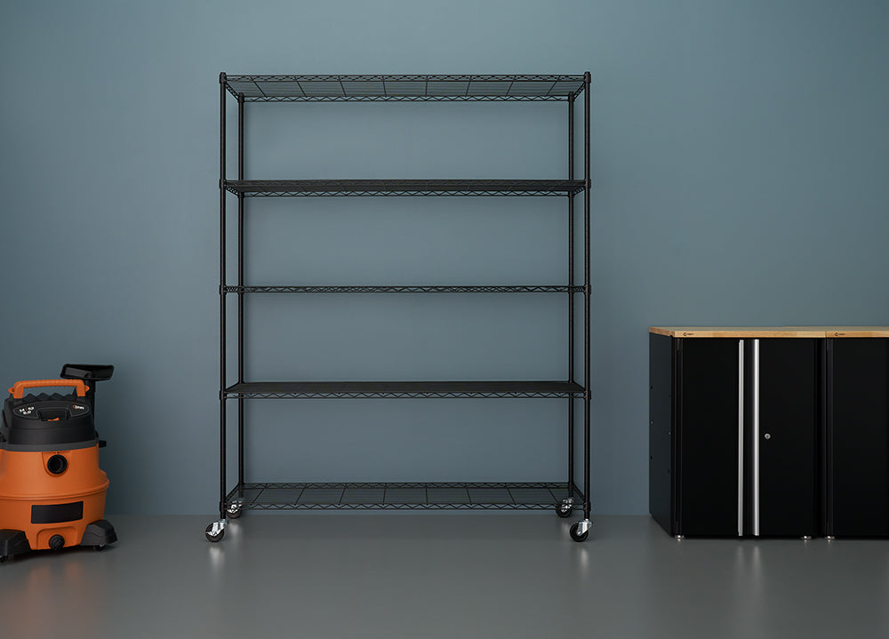 A black, five-tier wire shelving unit on casters stands against a solid blue-gray wall in a garage or workshop. To the left is an orange and black wet/dry shop vacuum, and to the right is a black storage cabinet with a wood-look top.