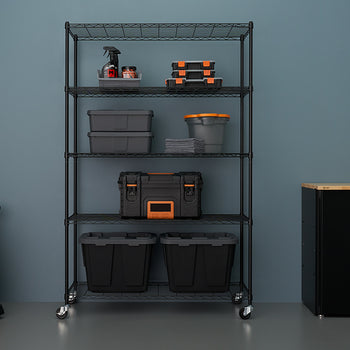 A tall, five-tier black wire shelving unit with casters is centered against a muted blue wall, fully organized with various black and grey storage bins, toolboxes, and cleaning supplies. To the left is an orange and black wet/dry vacuum, and to the right is a black cabinet with a light wood top.