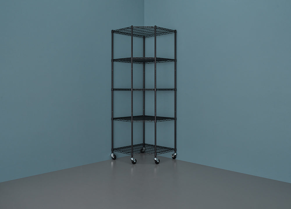 A five-tier, black wire corner shelving unit with casters sits against a deep blue wall in a room with a gray floor. The shelves are wide at the back and taper to a point in the front, fitting neatly into the corner.