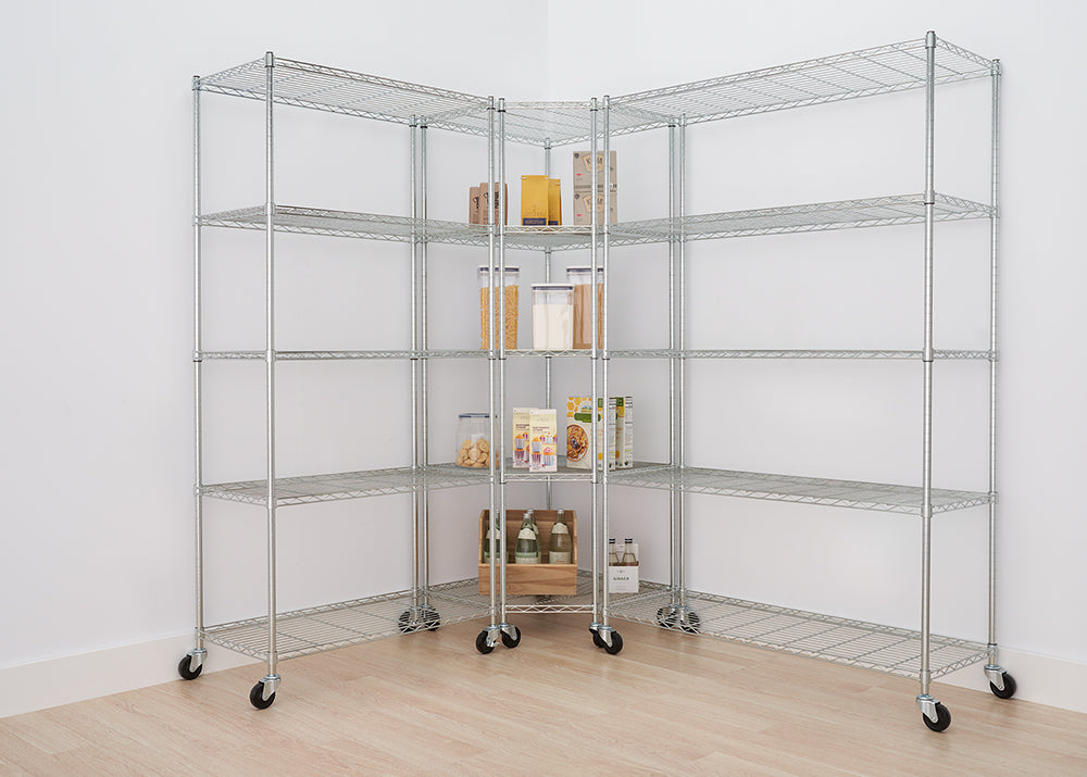 A two-unit chrome wire shelving system is assembled in the corner of a room, creating an L-shape with five shelves each. The shelves are on casters and hold various pantry items like cereal, flour, snacks, and bottles.