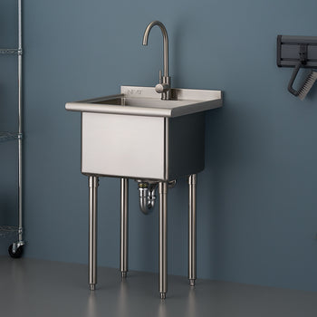 A commercial-style stainless steel utility sink with a gooseneck faucet stands on four metal legs in a garage or workshop setting. The sink is positioned against a blue-gray wall with a storage shelf unit visible on the left and cleaning tools hanging on the right.