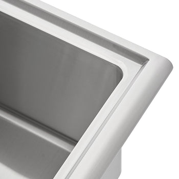 A close-up shot shows the corner of a brushed stainless steel sink. The image highlights the smooth, rounded edge of the rim and the clean, polished interior of the basin.