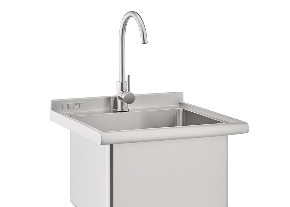 A close-up photograph shows a stainless steel outdoor utility sink featuring a high-arc chrome faucet mounted on the backsplash. The modern, square-shaped sink has rounded edges and the word "NEAT" etched into the backsplash.