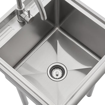 A high-angle close-up shot of a stainless steel utility sink with sharply defined, straight sides and a centered basket strainer in the drain. A gooseneck faucet is installed on the small, grooved drainboard area to the left of the main basin.