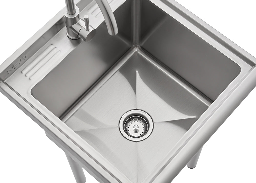 A high-angle close-up shot of a stainless steel utility sink with sharply defined, straight sides and a centered basket strainer in the drain. A gooseneck faucet is installed on the small, grooved drainboard area to the left of the main basin.
