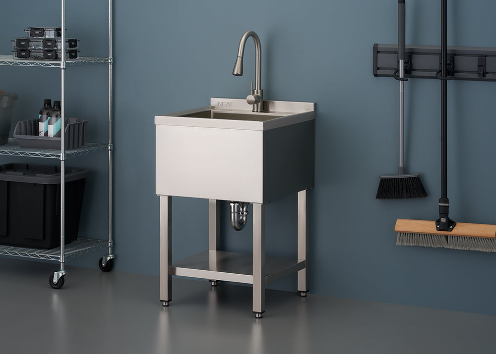 A close-up photograph features a stainless steel utility sink on a stand with a lower shelf, complete with a modern gooseneck faucet. The sink is set against a blue wall in what appears to be a garage or laundry room, with wire shelving on the left and cleaning tools hanging on the right.