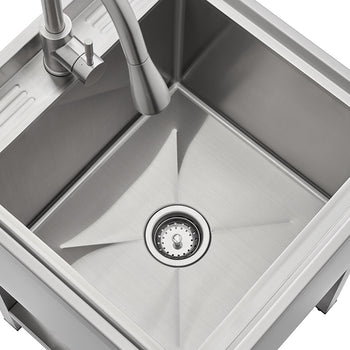 A high-angle close-up shows a modern stainless steel single-basin utility or laundry sink with a pull-down faucet. The sink has a squared shape and features a slightly recessed section with parallel ridges to the upper left.