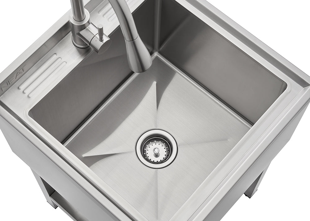 A high-angle close-up shows a modern stainless steel single-basin utility or laundry sink with a pull-down faucet. The sink has a squared shape and features a slightly recessed section with parallel ridges to the upper left.