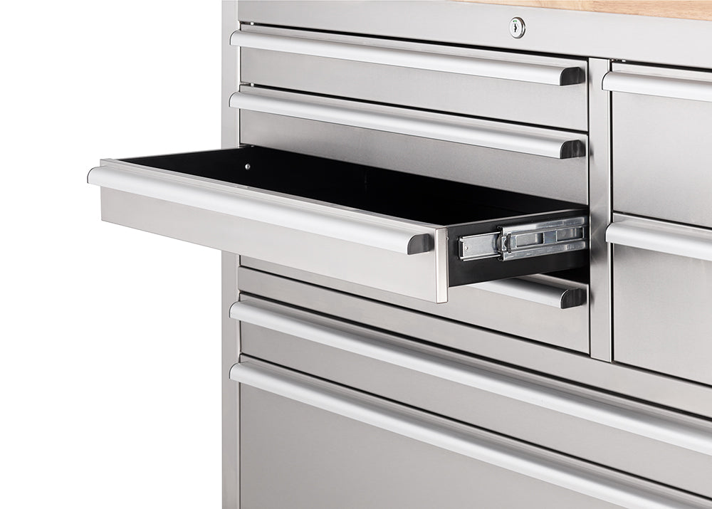 A close-up shot focuses on an open drawer of a stainless steel tool workbench, showing the smooth metal ball-bearing slide mechanism along its side. A cylinder key lock is visible above the top drawer.