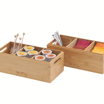 A front three-quarter view shows two natural bamboo storage organizers with four and three compartments respectively, positioned against a plain white background. Inside, they are neatly packed with various coffee and tea supplies, including K-Cups, stirrers, spice tins, and tea bags, and feature integrated handles for easy transport.