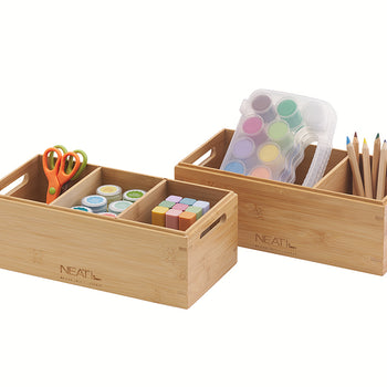 A natural wood desk organizer is filled with art and school supplies, including scissors, paint pots, a paint palette, and a bundle of colored pencils. The organizer has multiple compartments to hold the supplies neatly against a plain white background.