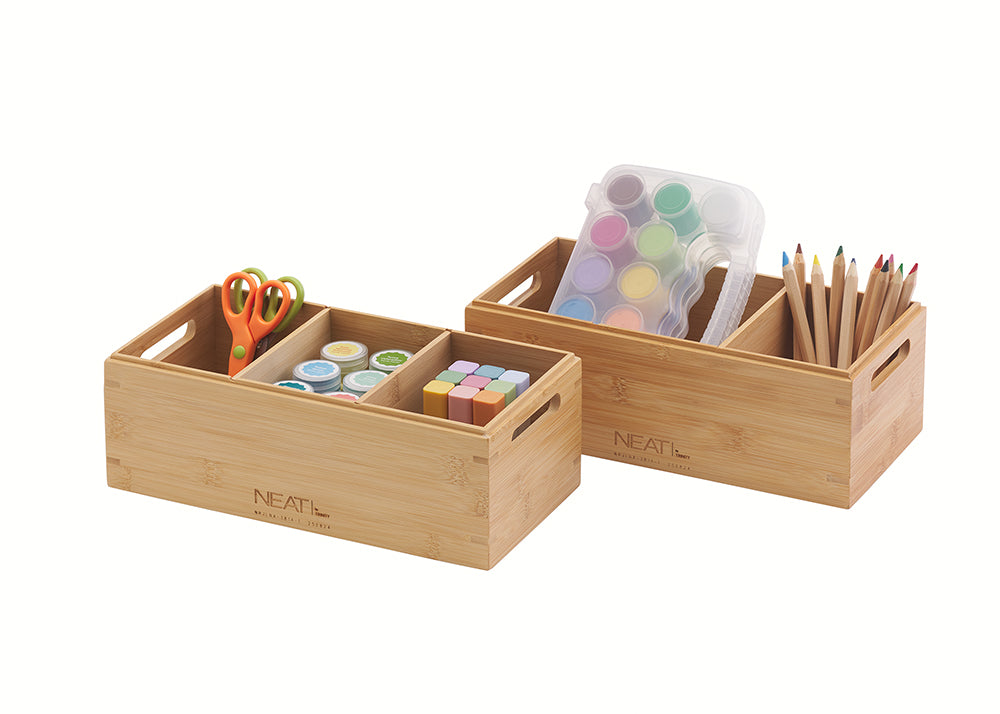 A natural wood desk organizer is filled with art and school supplies, including scissors, paint pots, a paint palette, and a bundle of colored pencils. The organizer has multiple compartments to hold the supplies neatly against a plain white background.