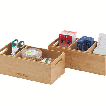 A natural wood multi-compartment desktop organizer is filled with various office and craft supplies, including scissors, a container of rubber bands, paper clips, staples, and note pads, against a plain white background. The organizer has integrated side handles for easy carrying.