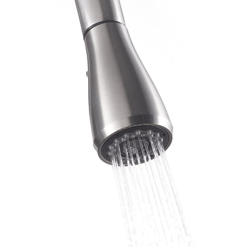 A close-up of a brushed stainless steel kitchen faucet sprayer head is shown, with water actively spraying downwards in a wide pattern. The sprayer head has several small nozzles visible, directing the streams of water.
