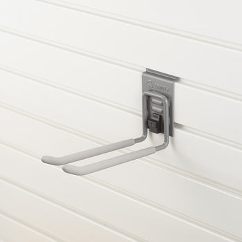 A gray utility hook with padded arms is mounted on a white slatwall panel. The hook has a locking mechanism labeled 