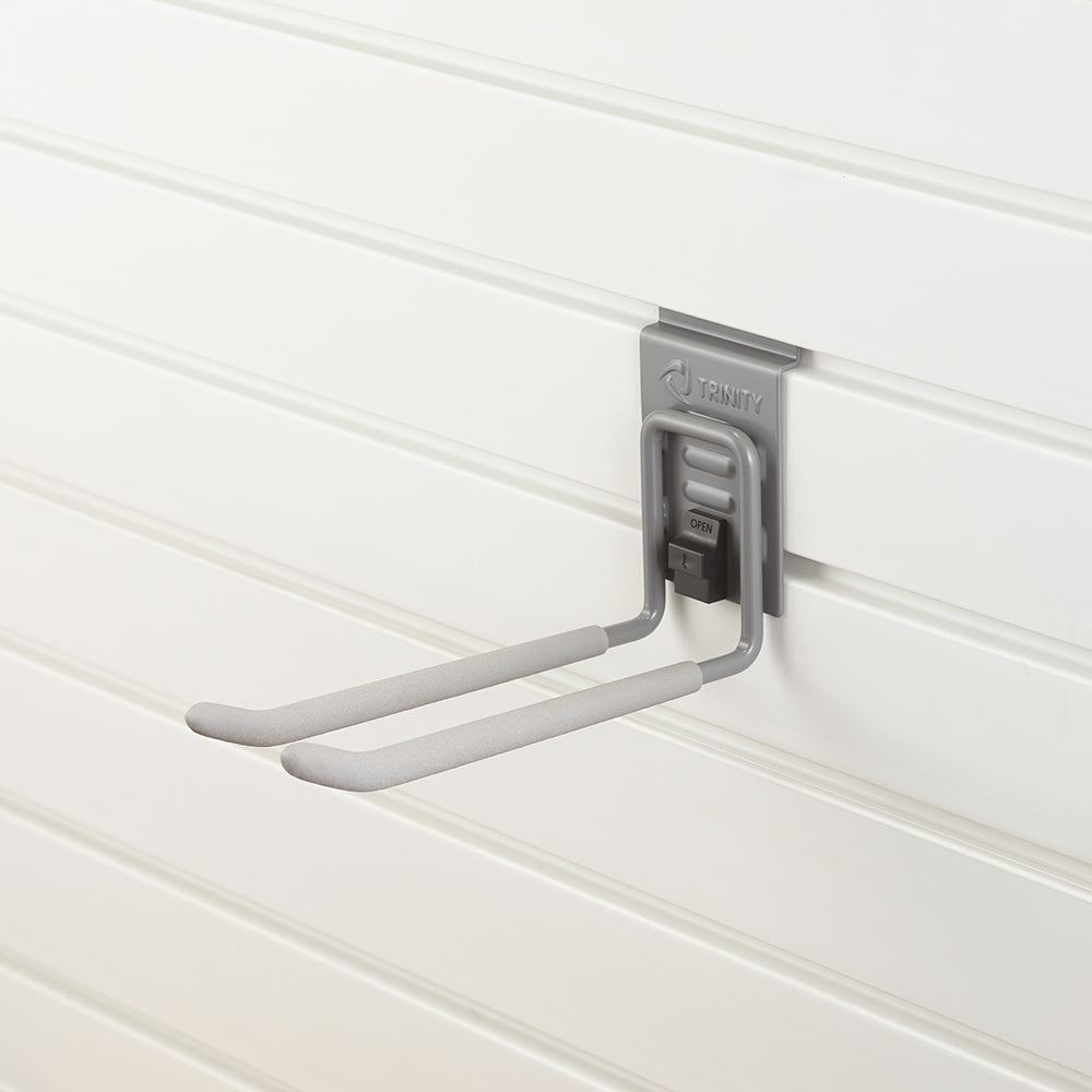 A gray utility hook with padded arms is mounted on a white slatwall panel. The hook has a locking mechanism labeled "OPEN" and is designed for holding tools, equipment, or other items.
