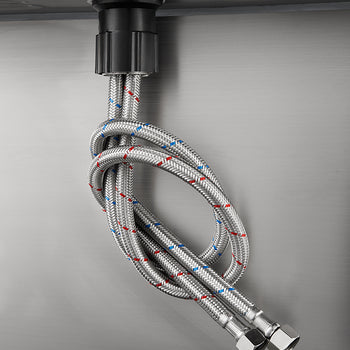 Two stainless steel braided flexible water supply hoses, one marked with a red stripe and one with a blue stripe, are attached to the base of a faucet on the underside of a sink or countertop. The hoses are tied in a loose knot and hang down, ending in metal female connectors.